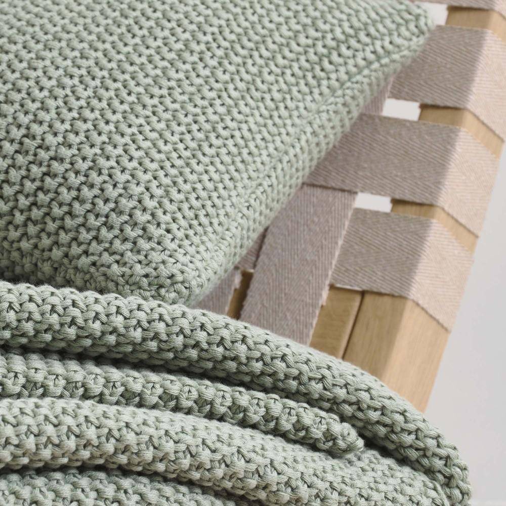 Marc O Polo Dekokissen Nordic Knit Garden Green mit Strickdecke im Detail auf Holzstuhl aus Bio Baumwolle in grünem Farbton