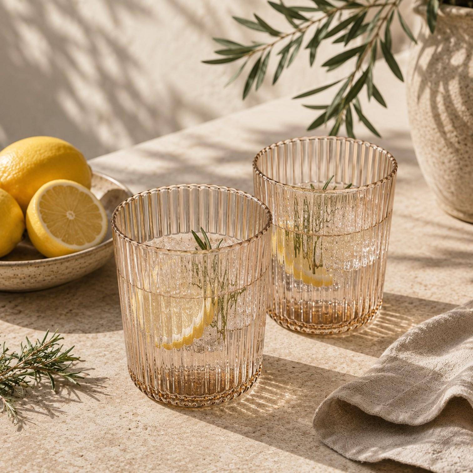 Paveau Ribbed Trinkgläser aus geriffeltem Glas stilvoll gedeckt auf einem sommerlichen Tisch mit Zitronen und Wasser