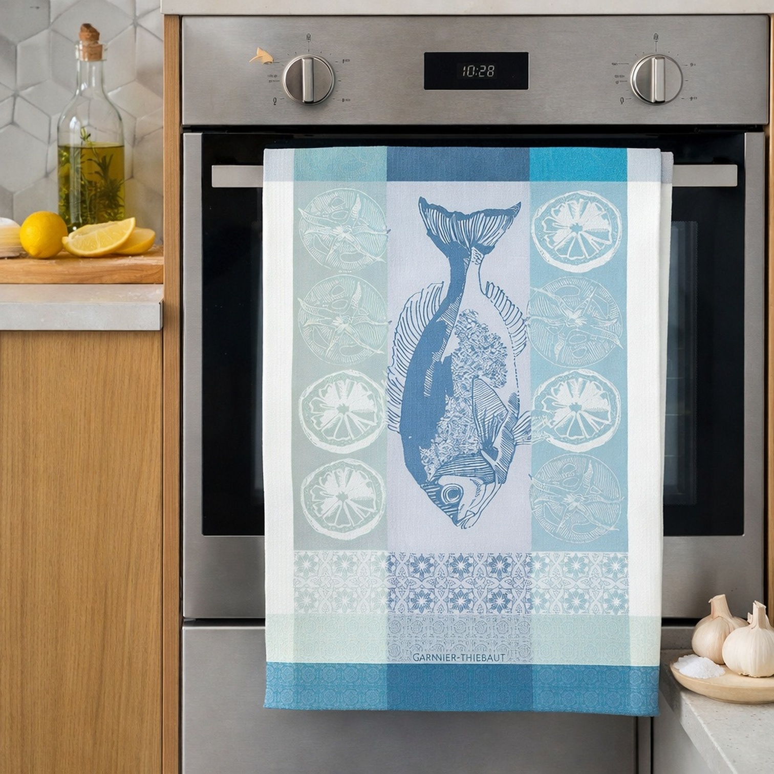 Plancha Outremer - Mediterranes Geschirrtuch mit Fischmotiv in Blau hängt dekorativ am Backofen in einer modernen Küche