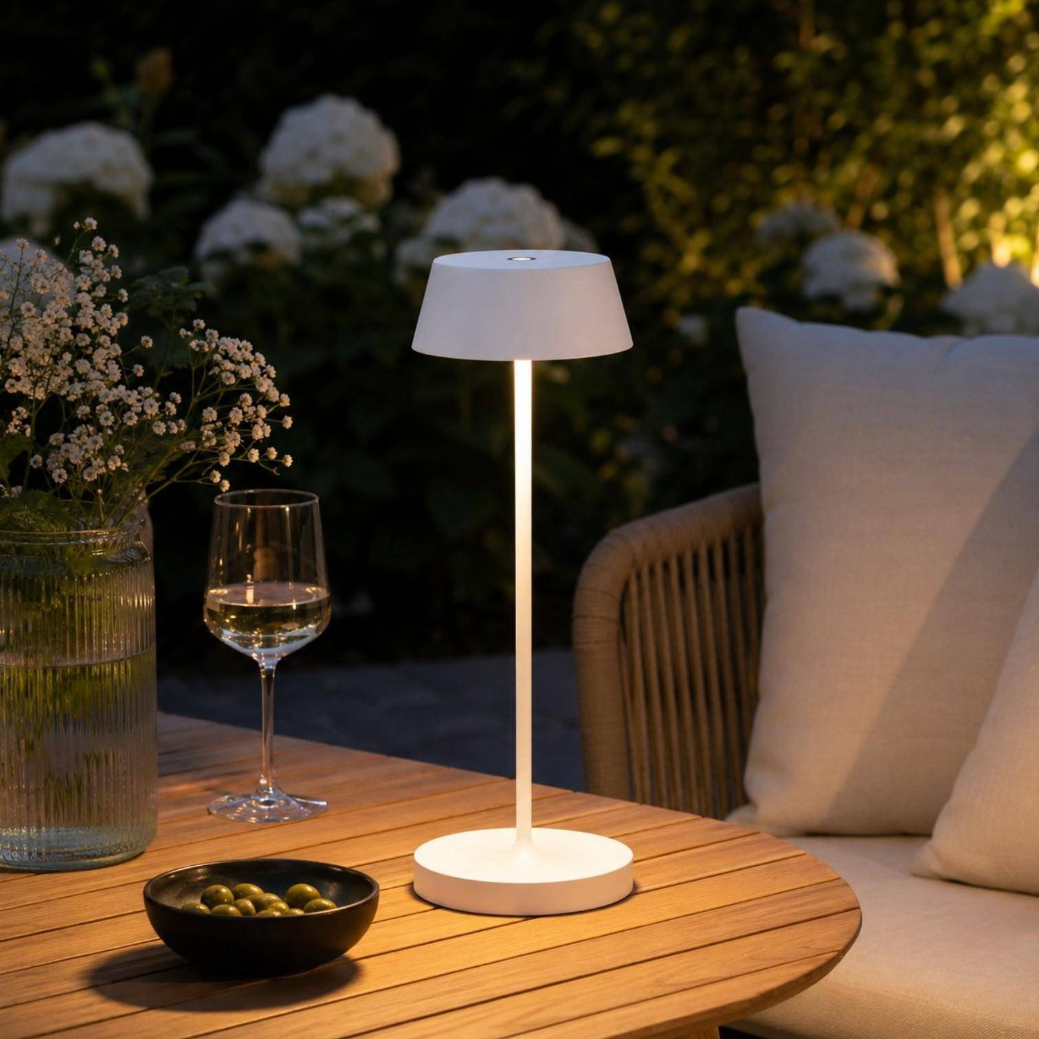 QOOZII Malta kabellose LED Tischlampe in Weiß auf einem Holztisch im Garten. Moderne Akku-Tischlampe mit warmweißem Licht für Terrasse, Balkon und Outdoor-Lounge.