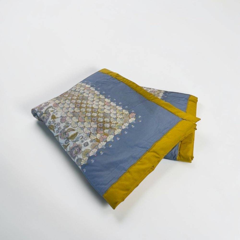 Gefaltetes Bassetti Plaid Tigullio C1 in Iceblue mit floralen Ornamenten und goldgelbem Rand auf hellem Hintergrund