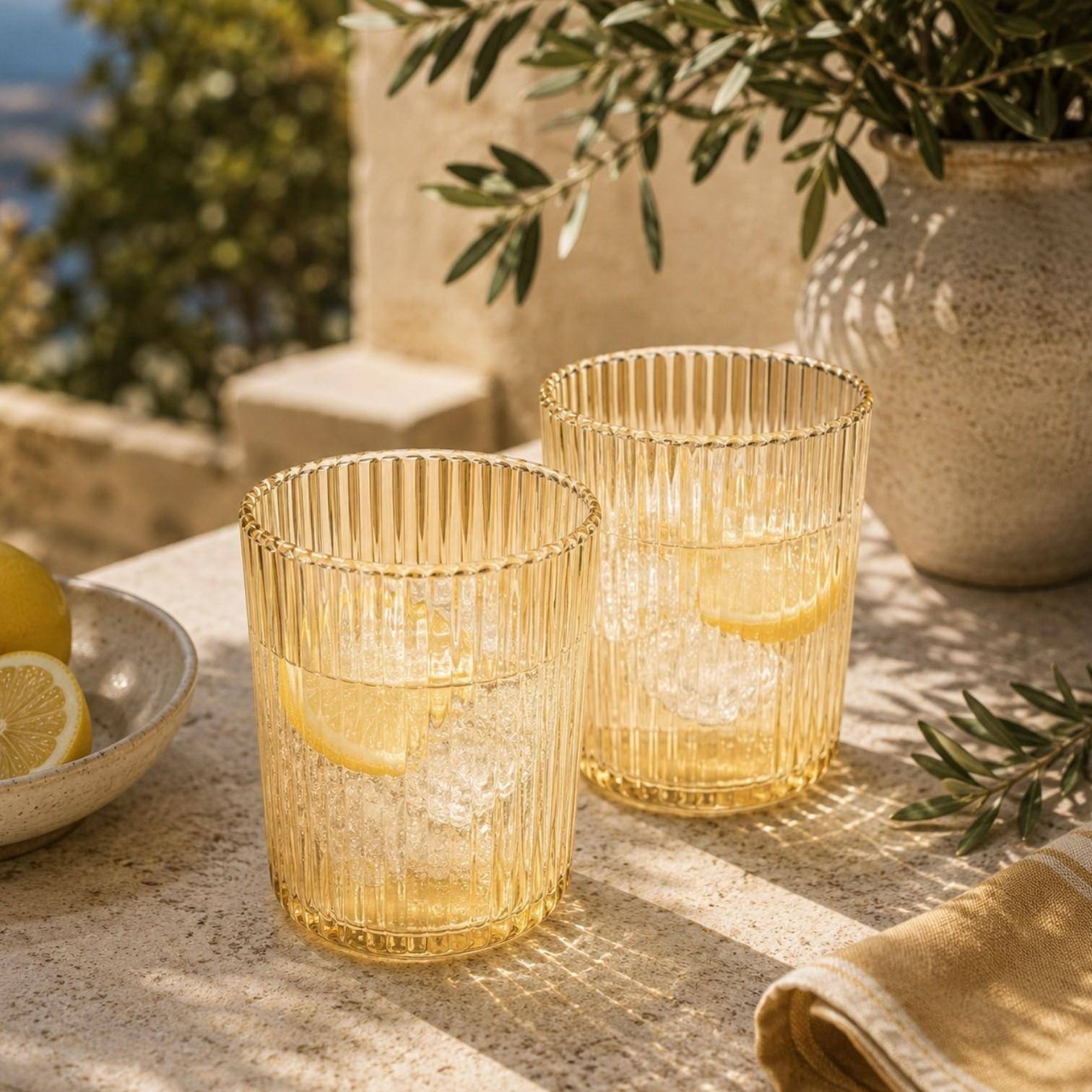 Paveau Ribbed Trinkgläser aus geriffeltem Glas stilvoll gedeckt auf einem sommerlichen Tisch mit Zitronen und Wasser