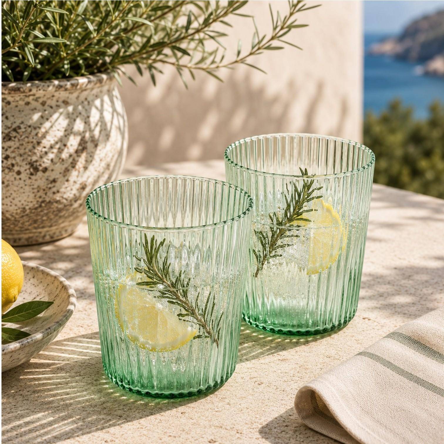 Paveau Ribbed Trinkgläser aus geriffeltem Glas stilvoll gedeckt auf einem sommerlichen Tisch mit Zitronen und Wasser