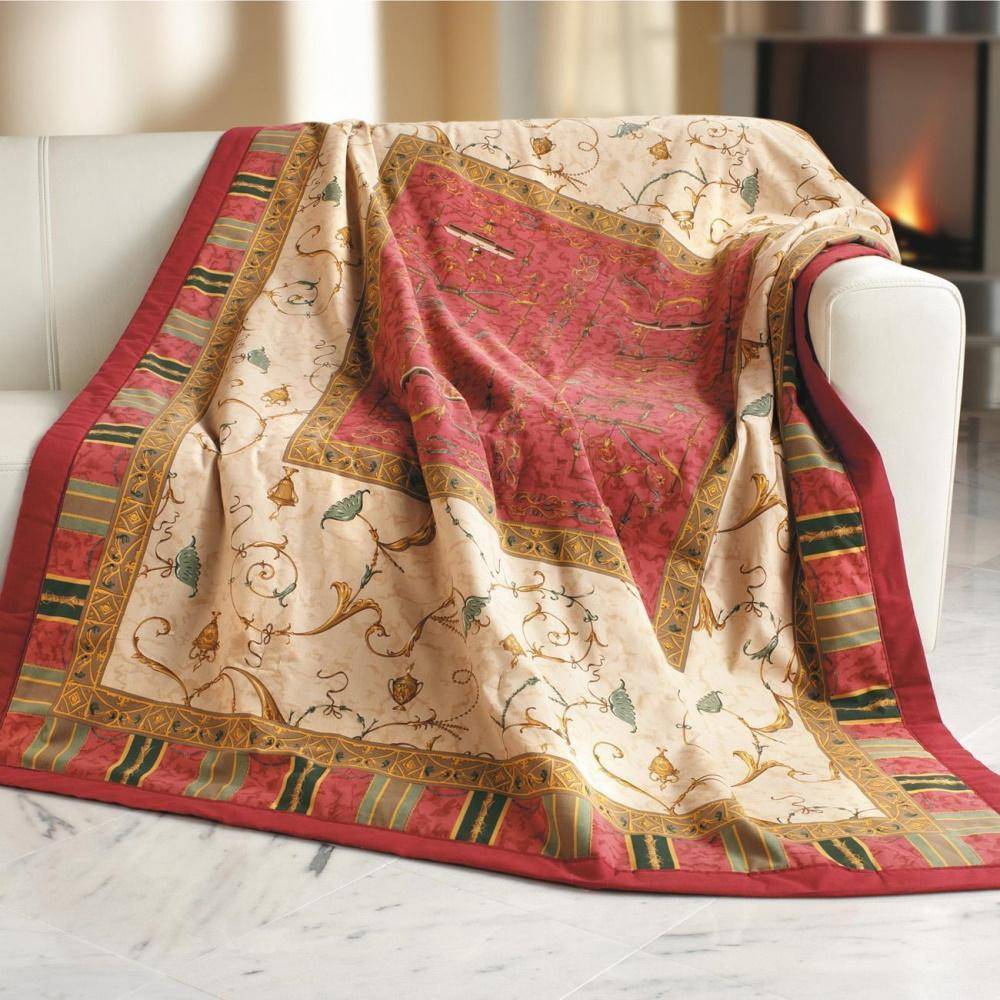 Bassetti Plaid Oplontis V8 in Beige-Rot dekorativ über ein Sofa gelegt, mit detailreichem floralen und ornamentalen Muster