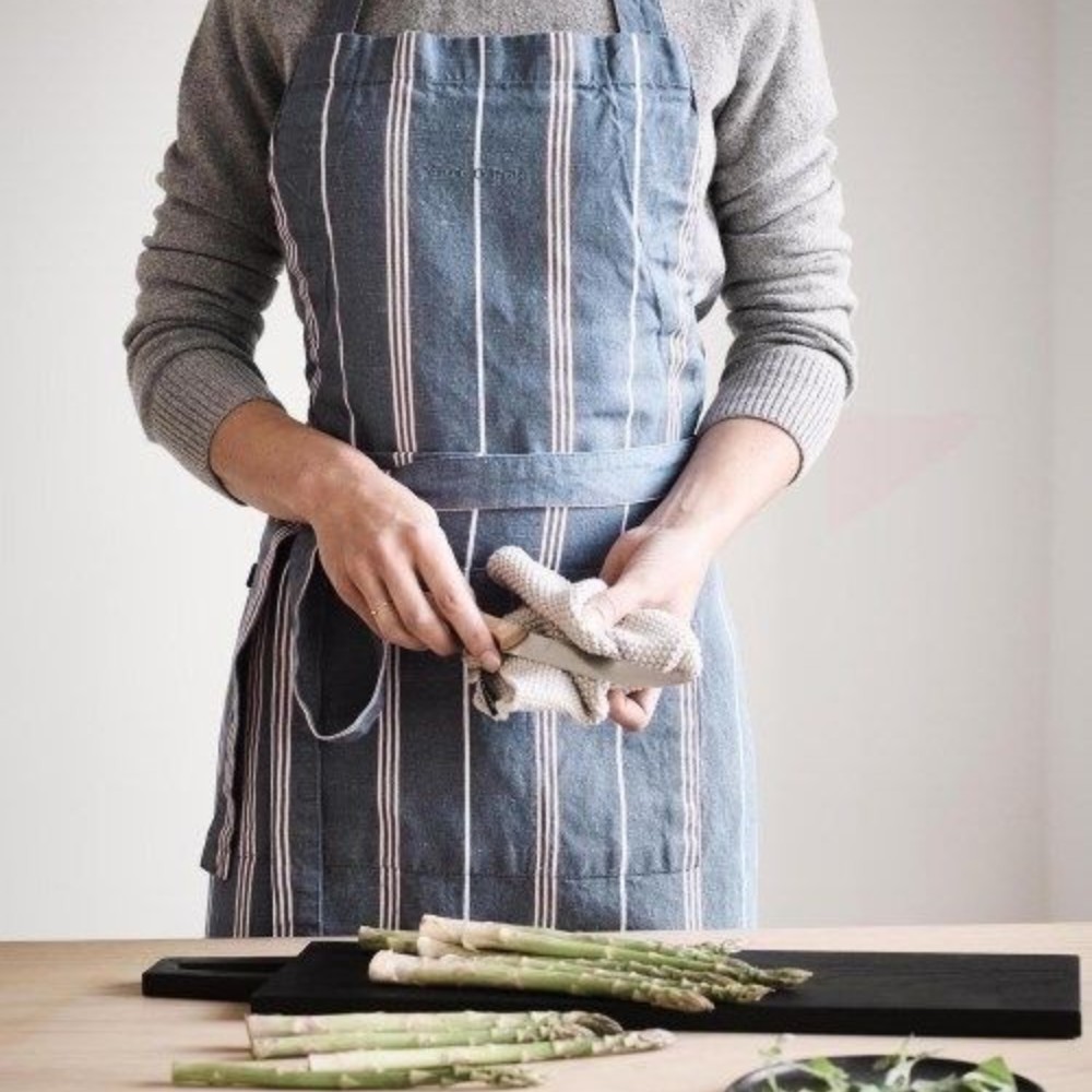 Person trägt die Marc O'Polo Schürze Jona Smoke Blue beim Kochen in moderner Küchenatmosphäre