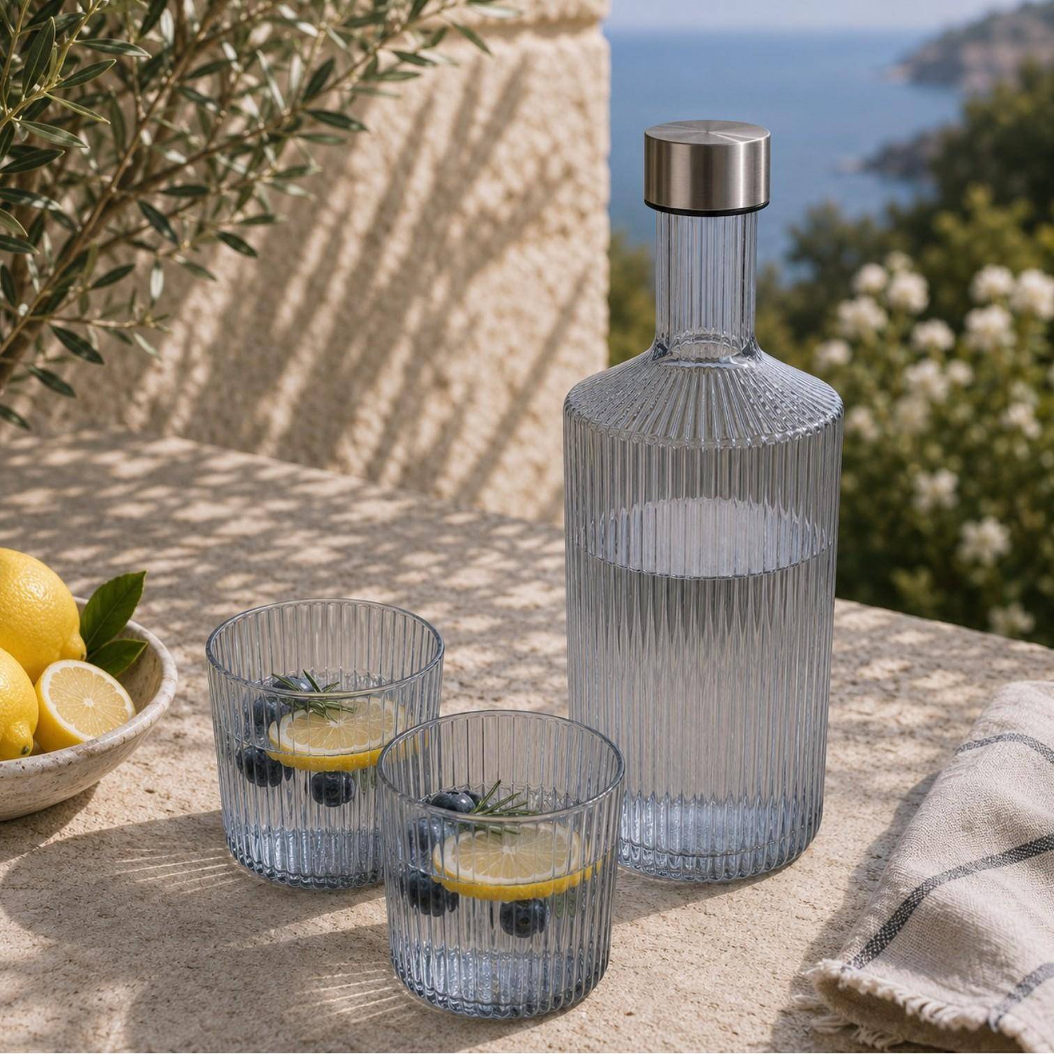 Paveau Ribbed Wasserflasche mit passenden Ribbed Gläsern auf einem sommerlich gedeckten Tisch im mediterranen Ambiente.