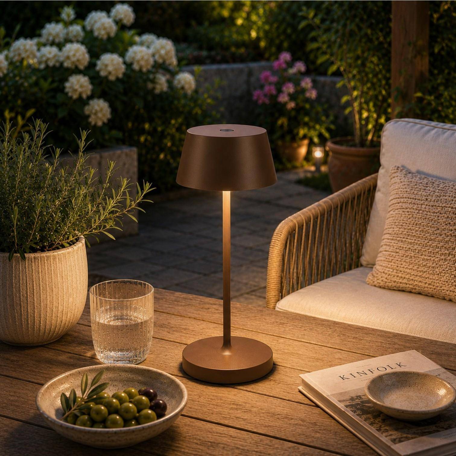 QOOZII Malta kabellose LED Tischlampe in Corten auf einem Holztisch im Garten. Moderne Akku-Tischlampe mit warmweißem Licht für Terrasse, Balkon und Outdoor-Lounge.