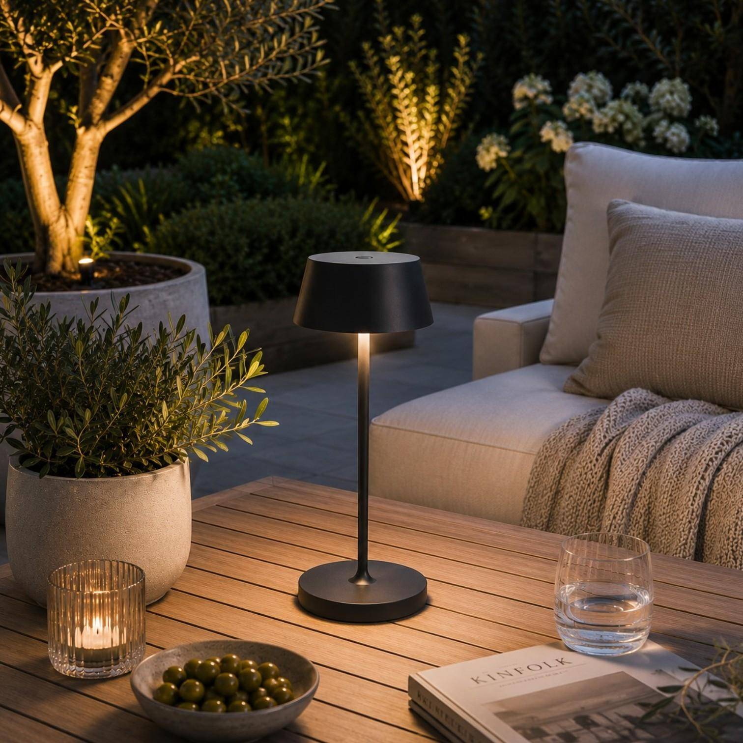 QOOZII Malta kabellose LED Tischlampe in Schwarz auf einem Holztisch im Garten. Moderne Akku-Tischlampe mit warmweißem Licht für Terrasse, Balkon und Outdoor-Lounge.